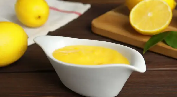Una ciotola bianca contiene una vellutata crema al limone, con limoni freschi sullo sfondo.
