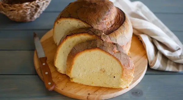 Pane di semola rustico, affettato su tagliere di legno, con coltello e tovagliolo a righe.