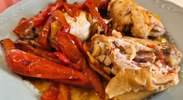 Pollo alla romana succulento con peperoni rossi arrostiti, servito su un piatto chiaro.