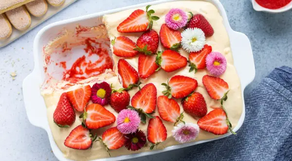 Tiramisù alle fragole ricetta originale: un dolce fresco e goloso, decorato con fragole fresche e piccoli fiori colorati.