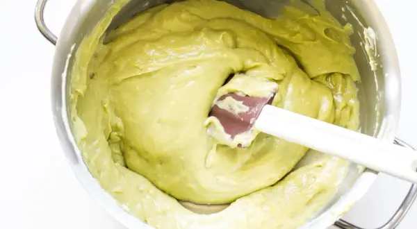 Una spatola mescola una densa crema al pistacchio in una ciotola d'acciaio.