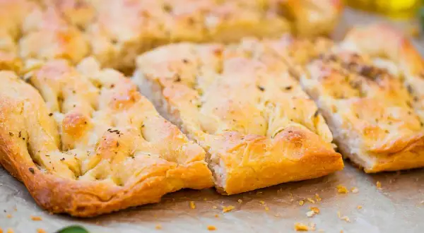 Focaccia senza lievito dorata e fragrante, tagliata a pezzi, con erbe aromatiche e un filo d'olio d'oliva.