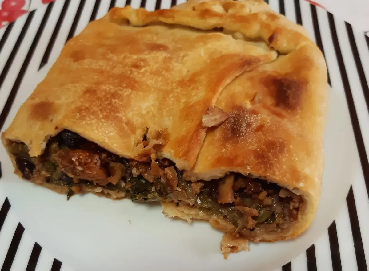 Una fetta di pizza di scarola, con ripieno di verdure e olive, su un piatto a righe bianche e nere.