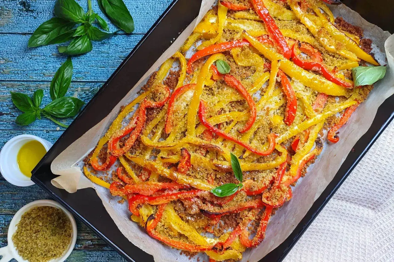 Peperoni al forno tagliati a listarelle, dorati e croccanti, conditi con pangrattato e basilico fresco.