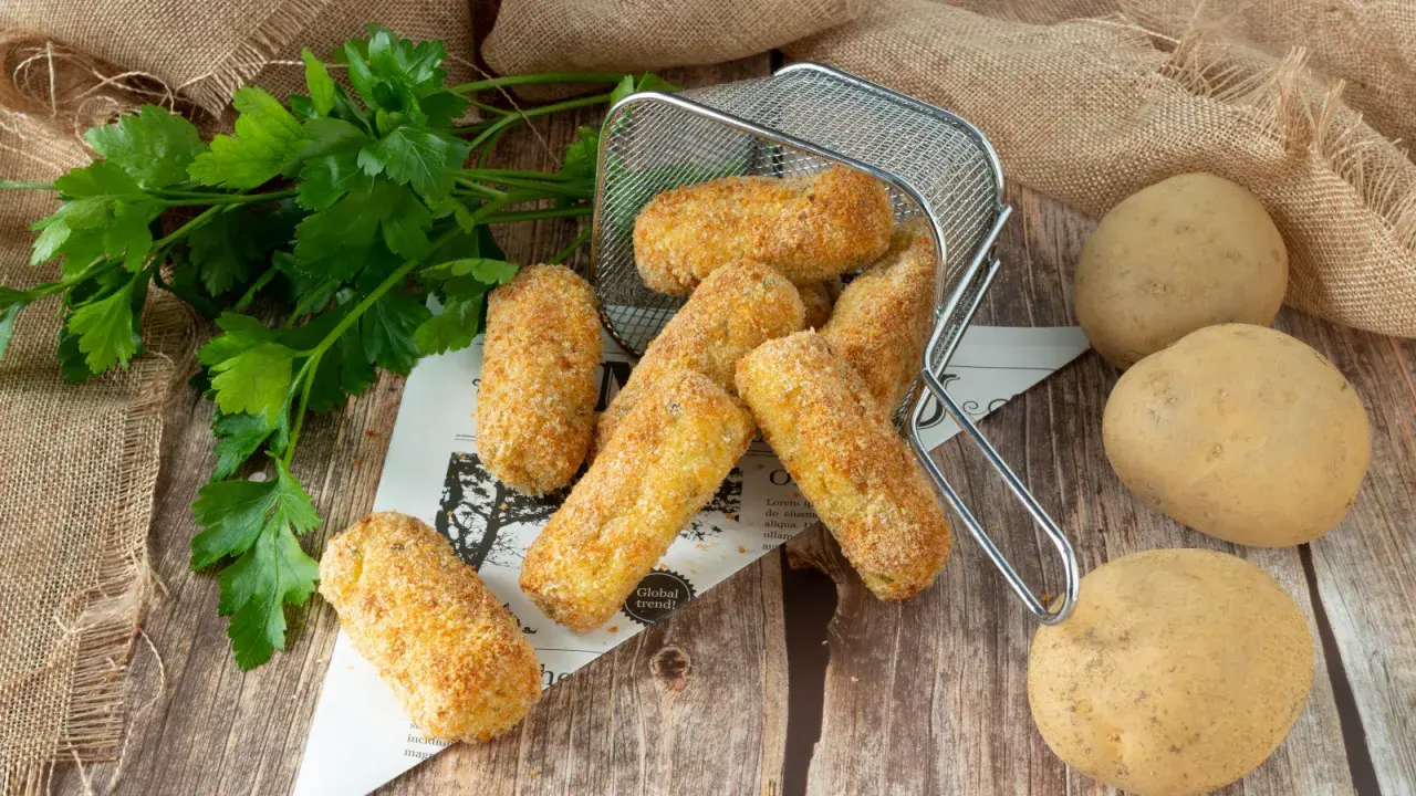 Crocchette di patate in friggitrice ad aria, dorate e croccanti, pronte per essere gustate. Accanto, patate fresche e prezzemolo.