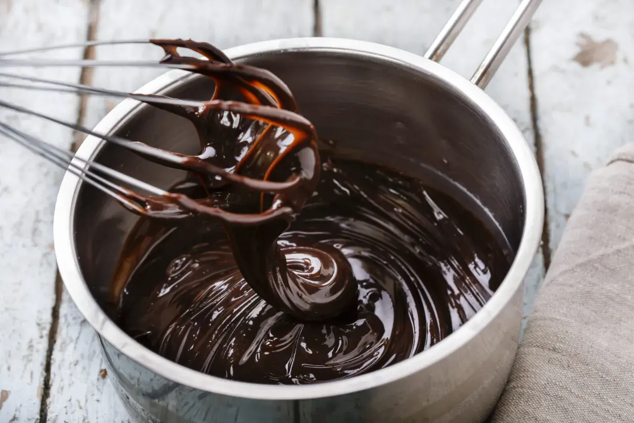 Una frusta mescola una lucida crema al cioccolato in una pentola d'acciaio.