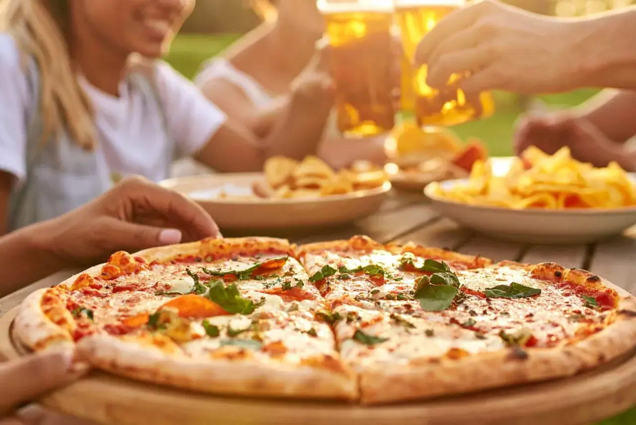 Una deliziosa pizza fatta in casa, tagliata a fette, pronta per essere gustata con amici e birra fresca all'aperto.