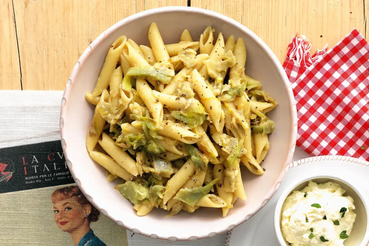 Penne con carciofi, un piatto che Antonino Cannavacciuolo saprebbe preparare alla perfezione, servito in una ciotola rosa.