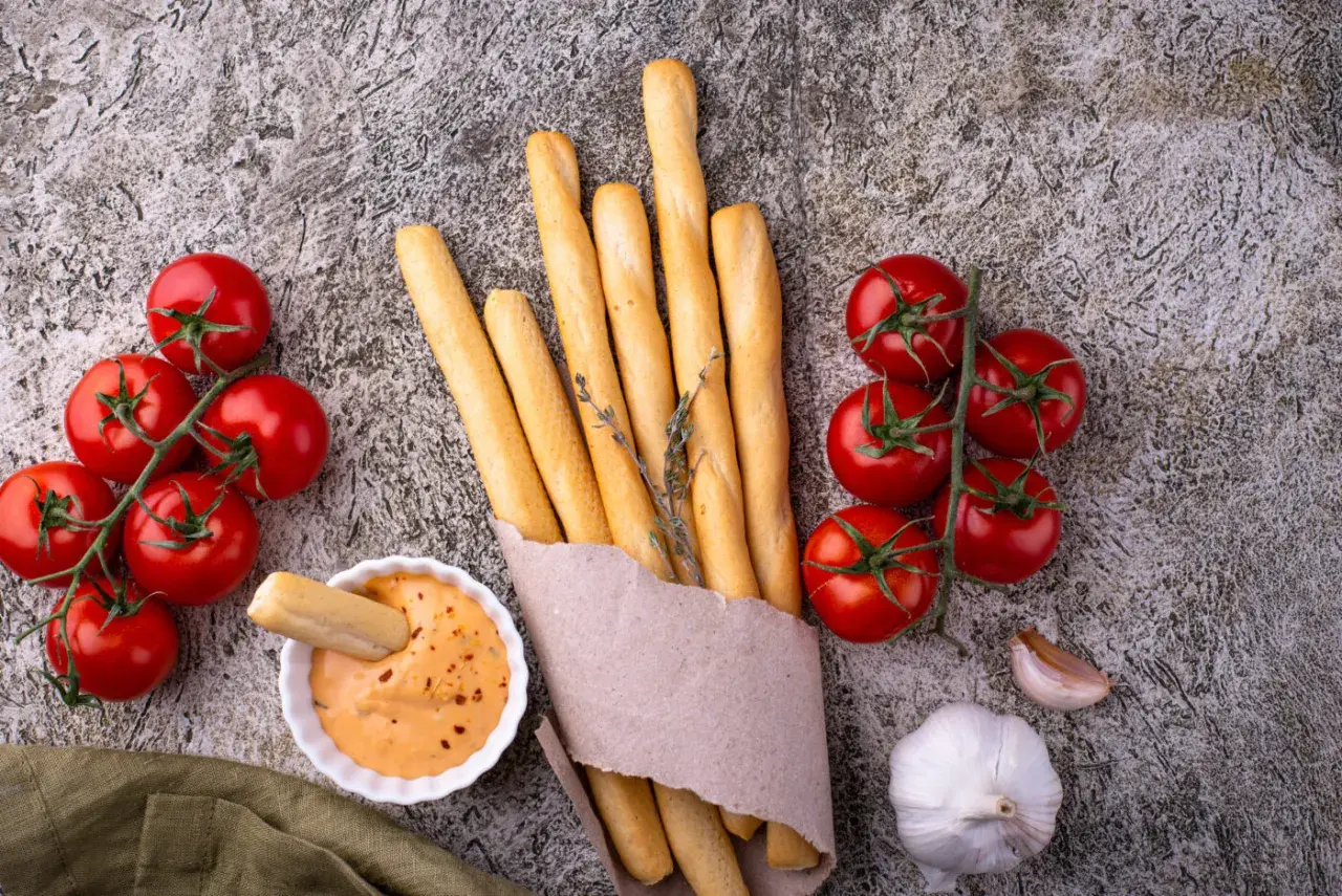Grissini fatti in casa dorati, con pomodorini freschi, aglio e una salsa cremosa. Perfetti per un aperitivo rustico.