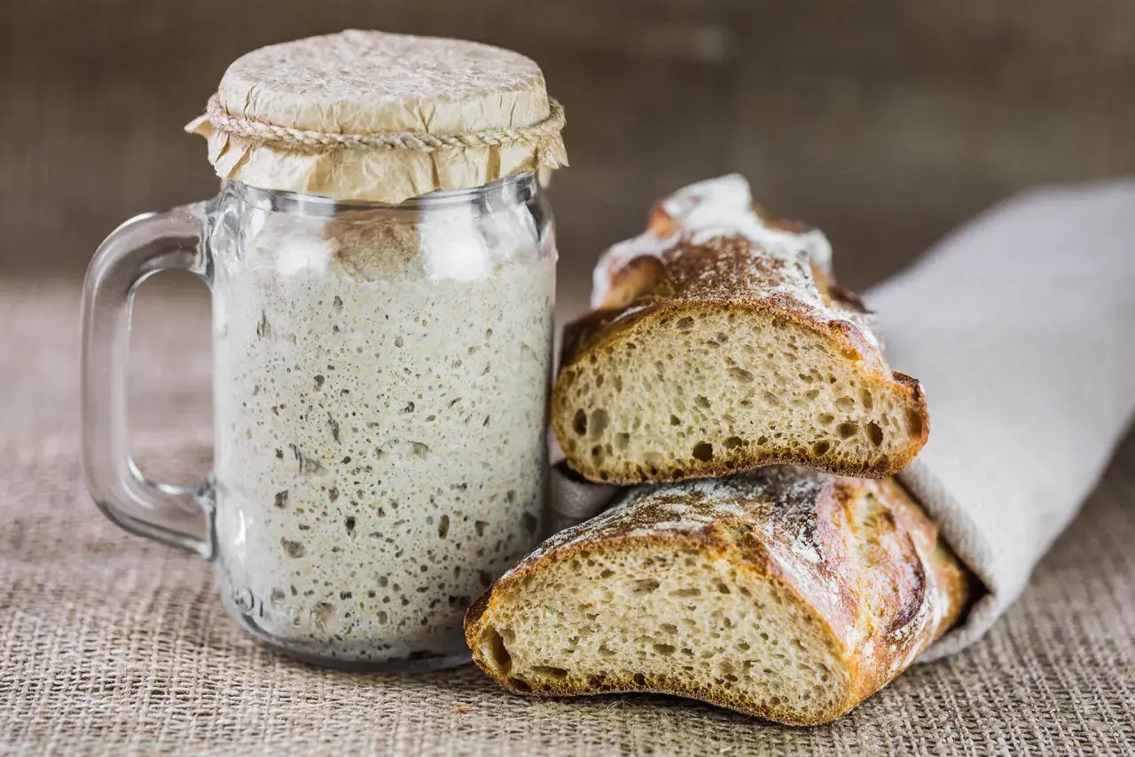 Un barattolo di lievito madre attivo e fette di pane rustico, pronti per creare deliziosi impasti. Ecco come si fa il lievito madre.