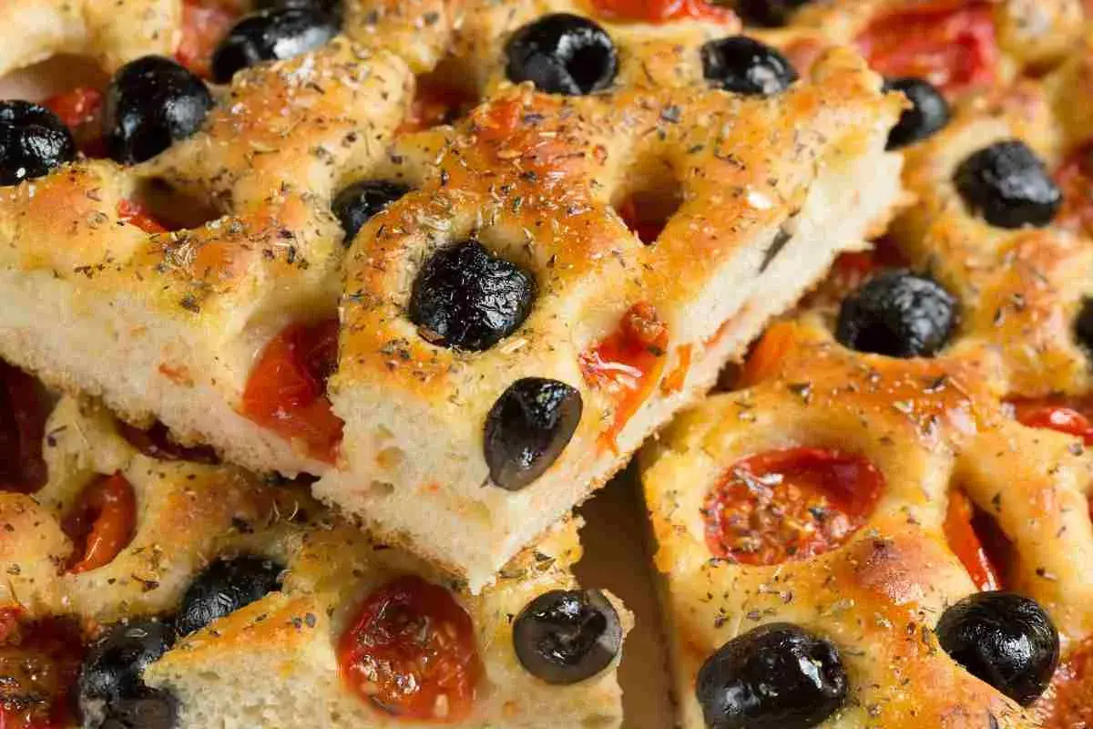 Focaccia pugliese ricetta originale sofficissima, con pomodorini e olive nere, condita con erbe aromatiche.