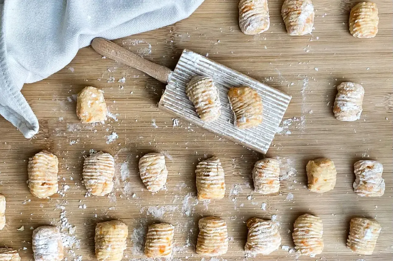 Gnocchi di zucca fatti in casa, pronti per essere cotti, sparsi su un tagliere di legno con un rigagnocchi.