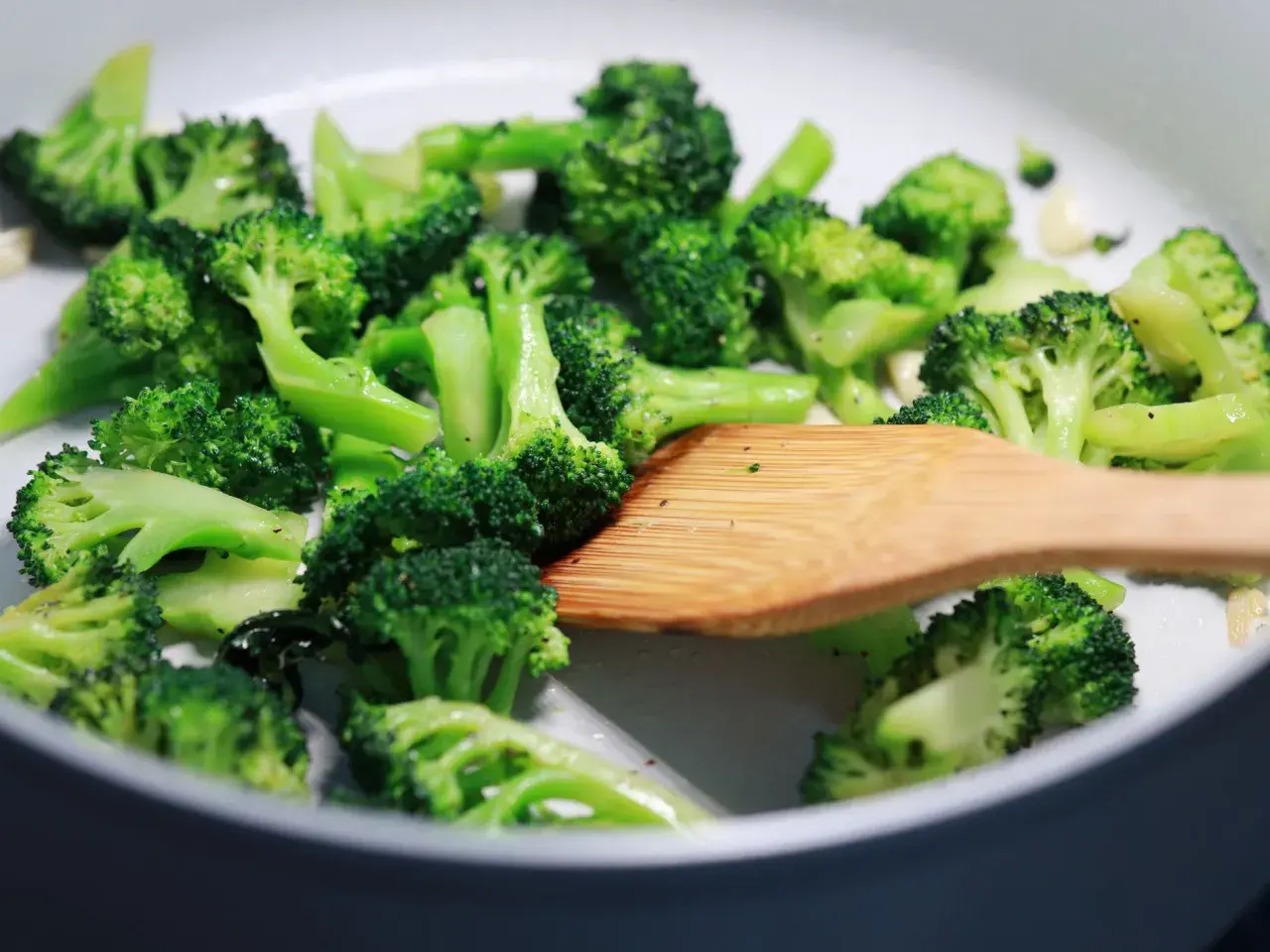 Broccoli in padella, con un mestolo di legno che mescola le cimette verdi e brillanti, pronte per essere gustate.