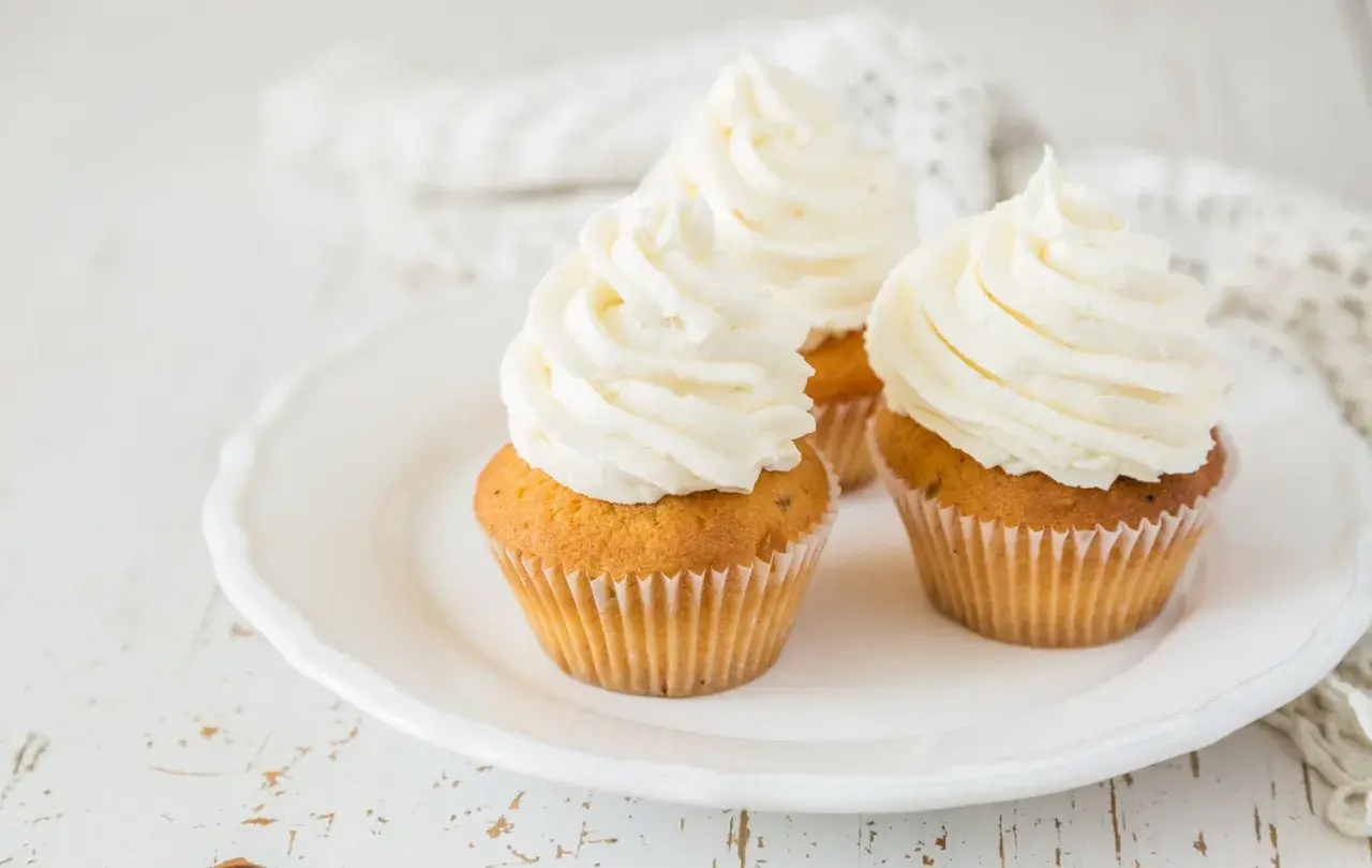 Tre cupcake su un piatto bianco, decorati con abbondante crema al burro soffice e ariosa.