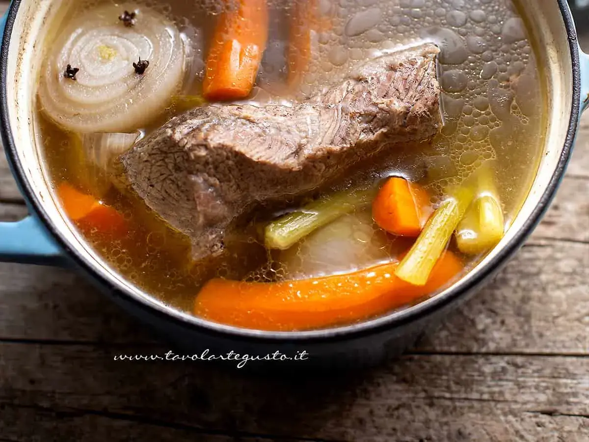 Un pezzo di carne succulenta cuoce lentamente in un brodo di carne aromatico, con carote, sedano e cipolla.