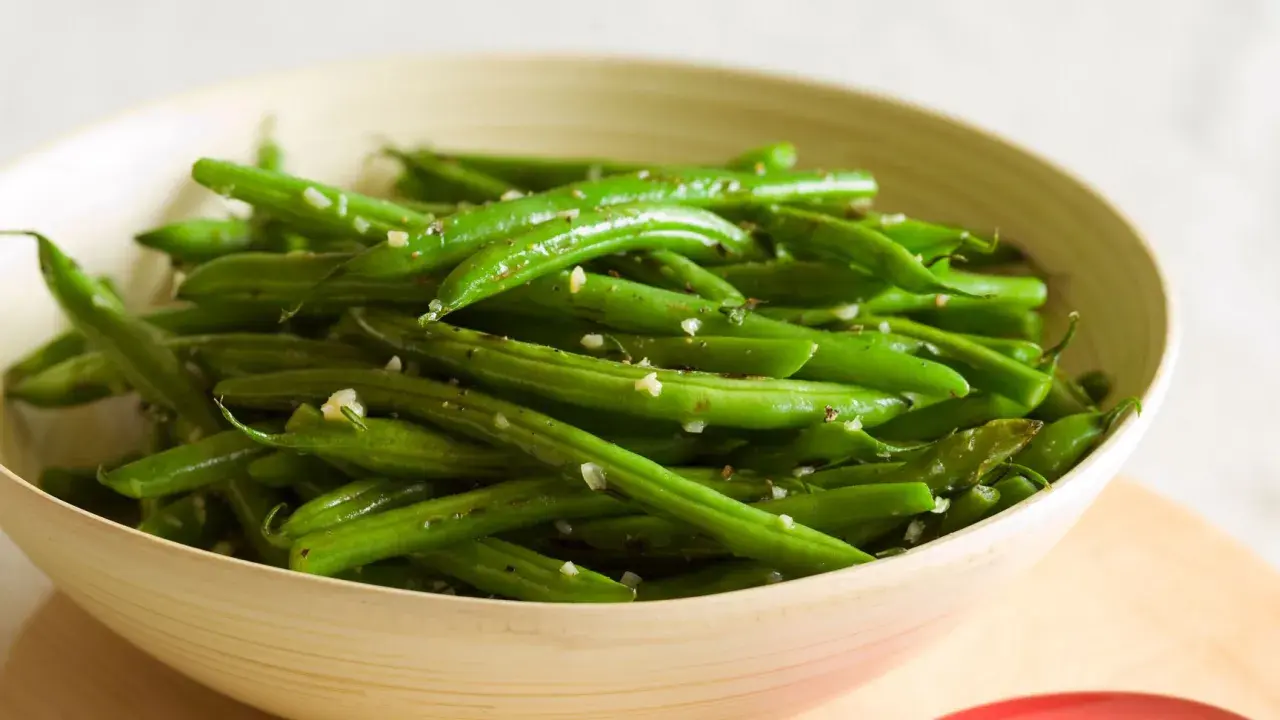 Fagiolini freschi saltati in padella con aglio e pepe, serviti in una ciotola di legno.