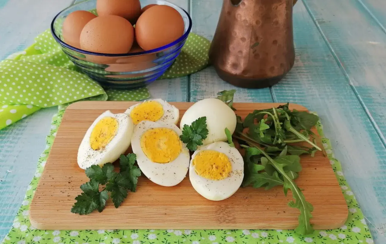 Uova sode in friggitrice ad aria, tagliate a metà, con un ciuffo di prezzemolo e rucola su un tagliere di legno.
