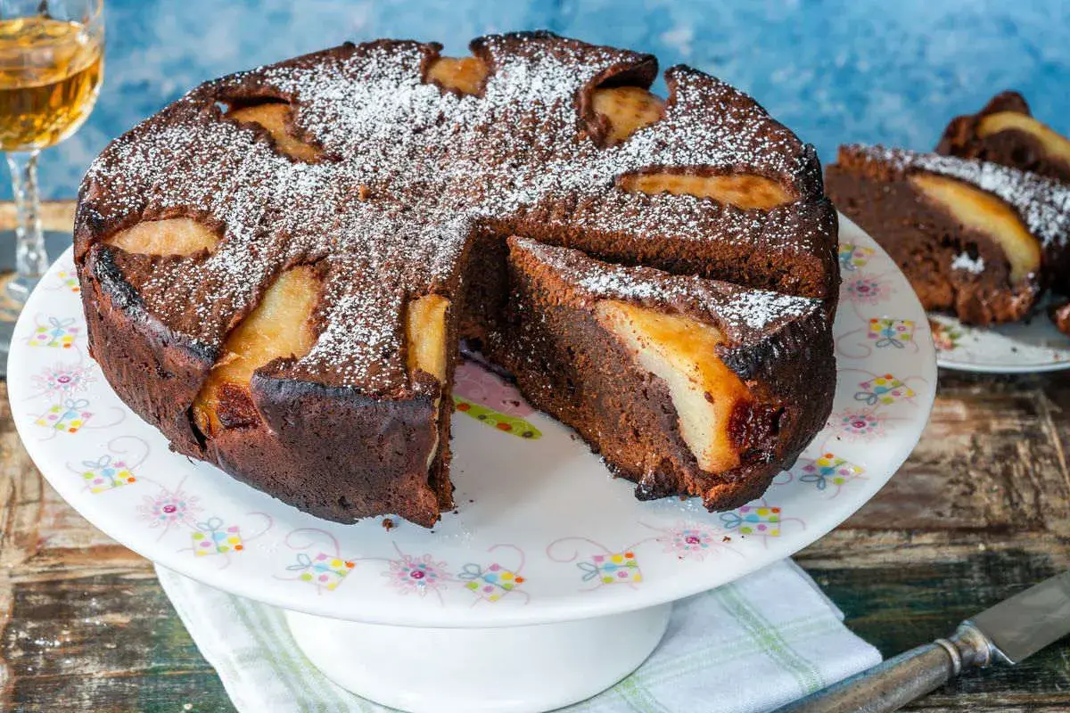 Torta al cioccolato e pere, cotta in friggitrice ad aria, spolverata di zucchero a velo. Una fetta è già servita.