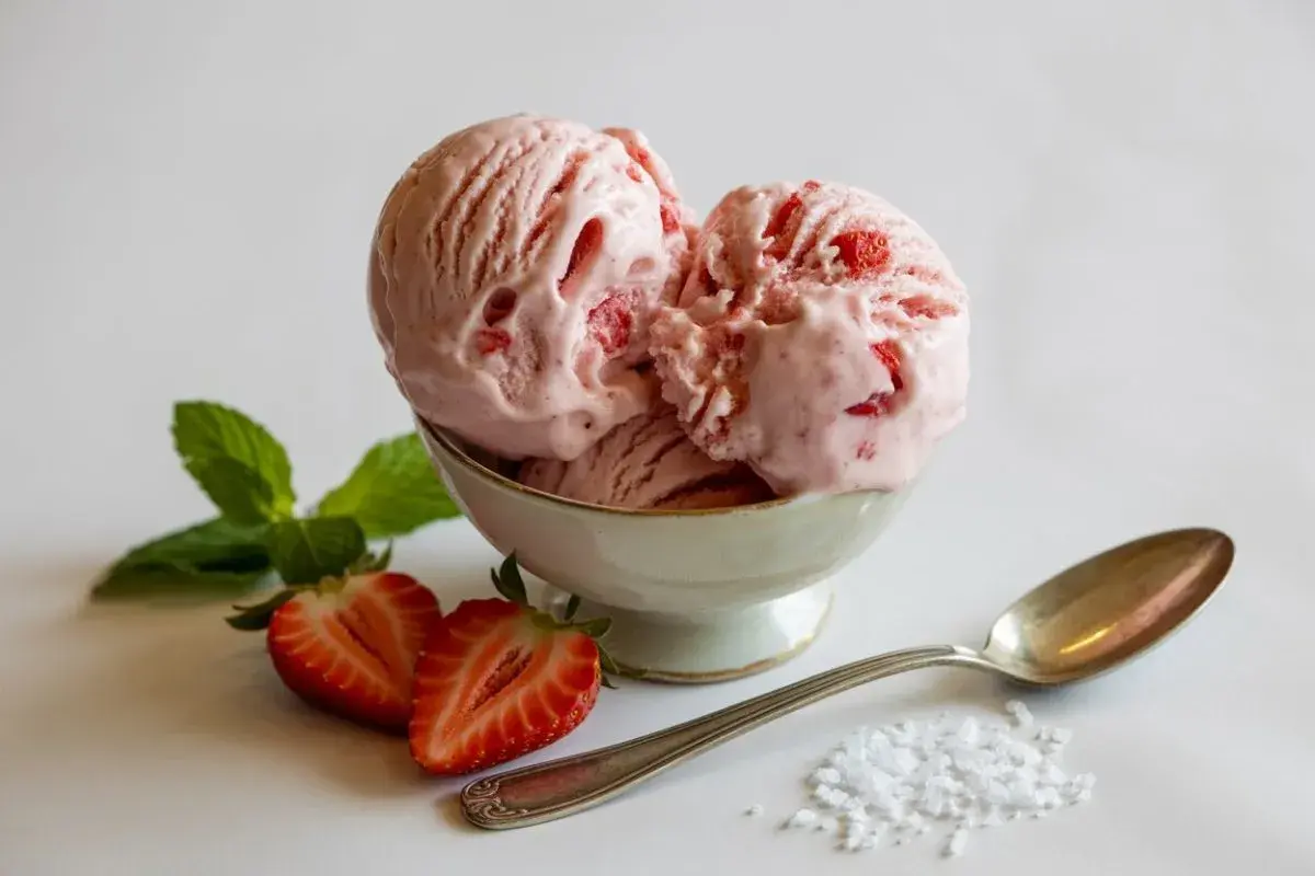 Coppa di cremoso gelato alla fragola, guarnita con fragole fresche e menta.