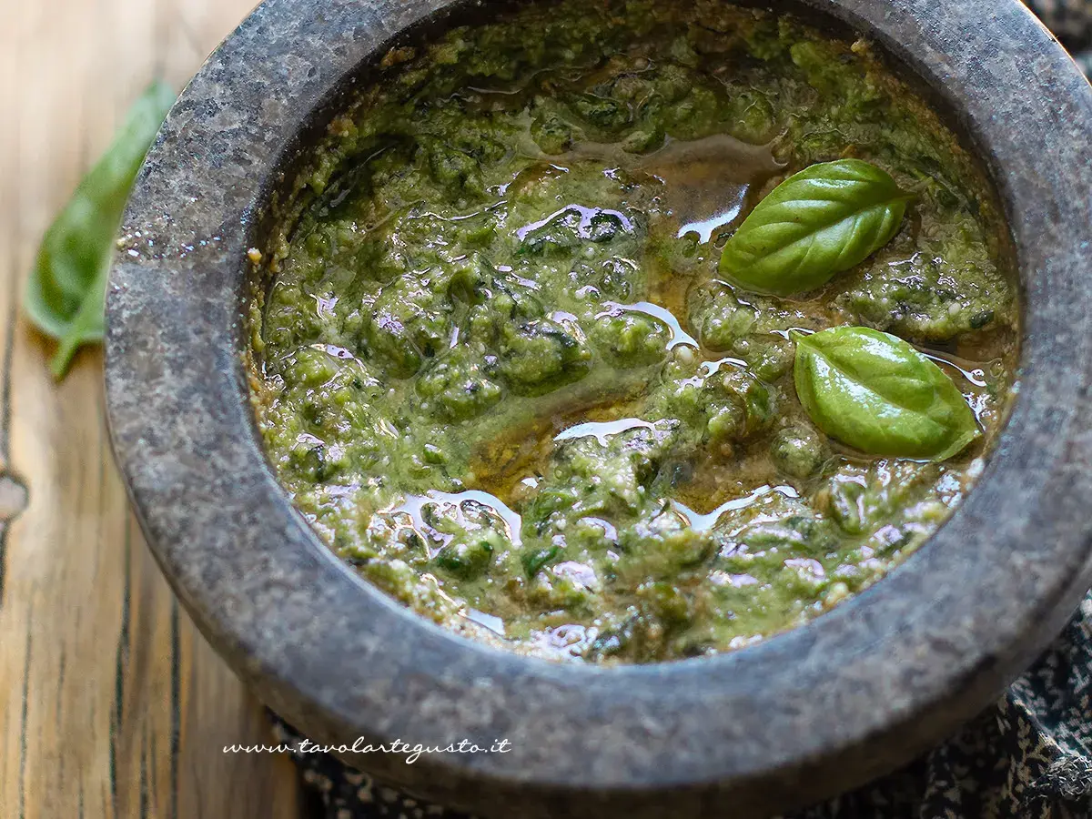 Pesto alla genovese appena preparato nel mortaio, con foglie di basilico fresco che galleggiano sull'olio.