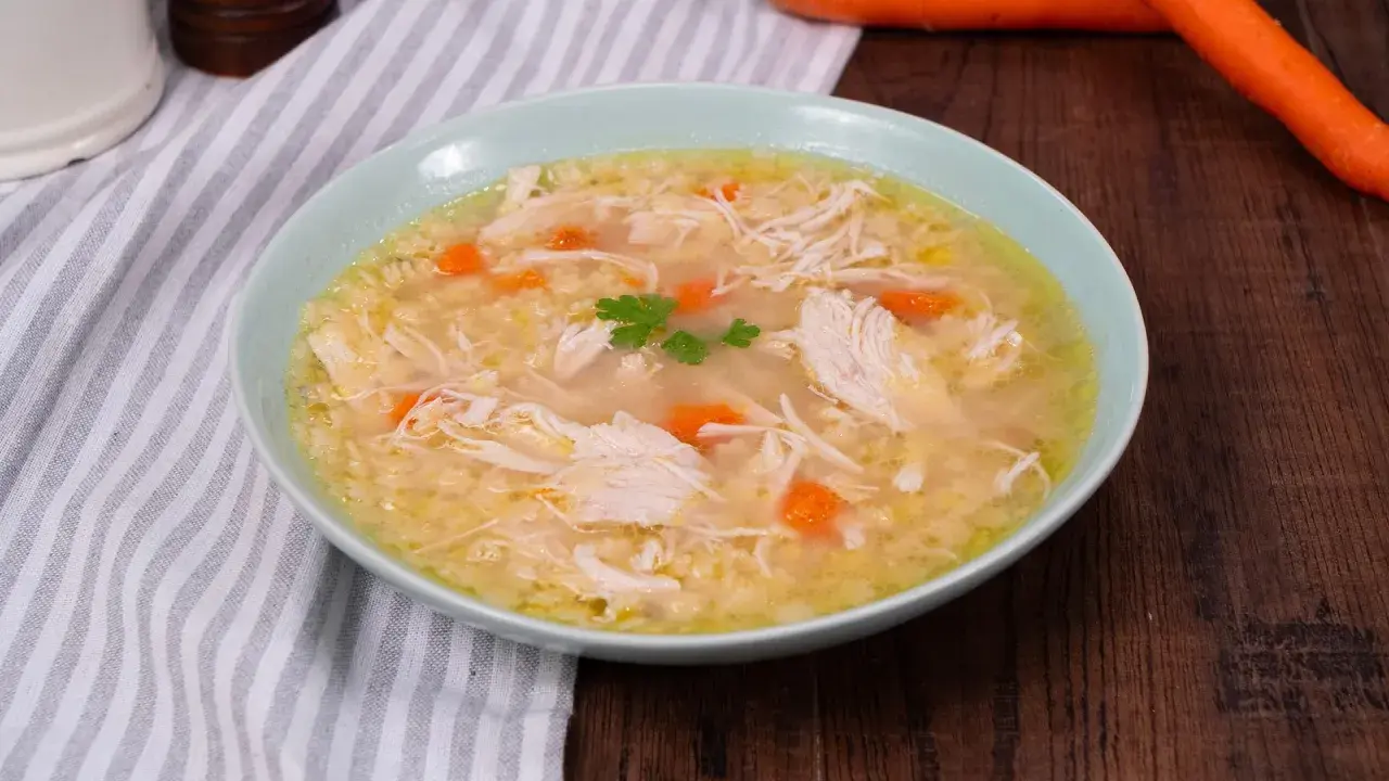 Un confortevole brodo di pollo con pezzi di pollo sfilacciato, carote e un rametto di prezzemolo.