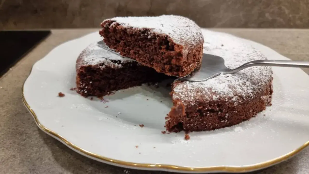 Una fetta di torta all'acqua al cacao, soffice e spolverata di zucchero a velo, viene sollevata da una spatola.