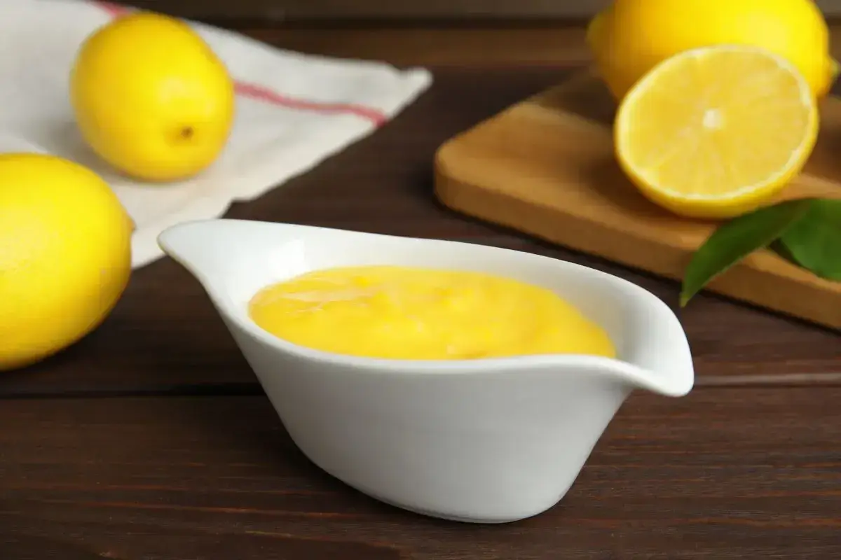Una ciotola bianca contiene una vellutata crema al limone, con limoni freschi sullo sfondo.