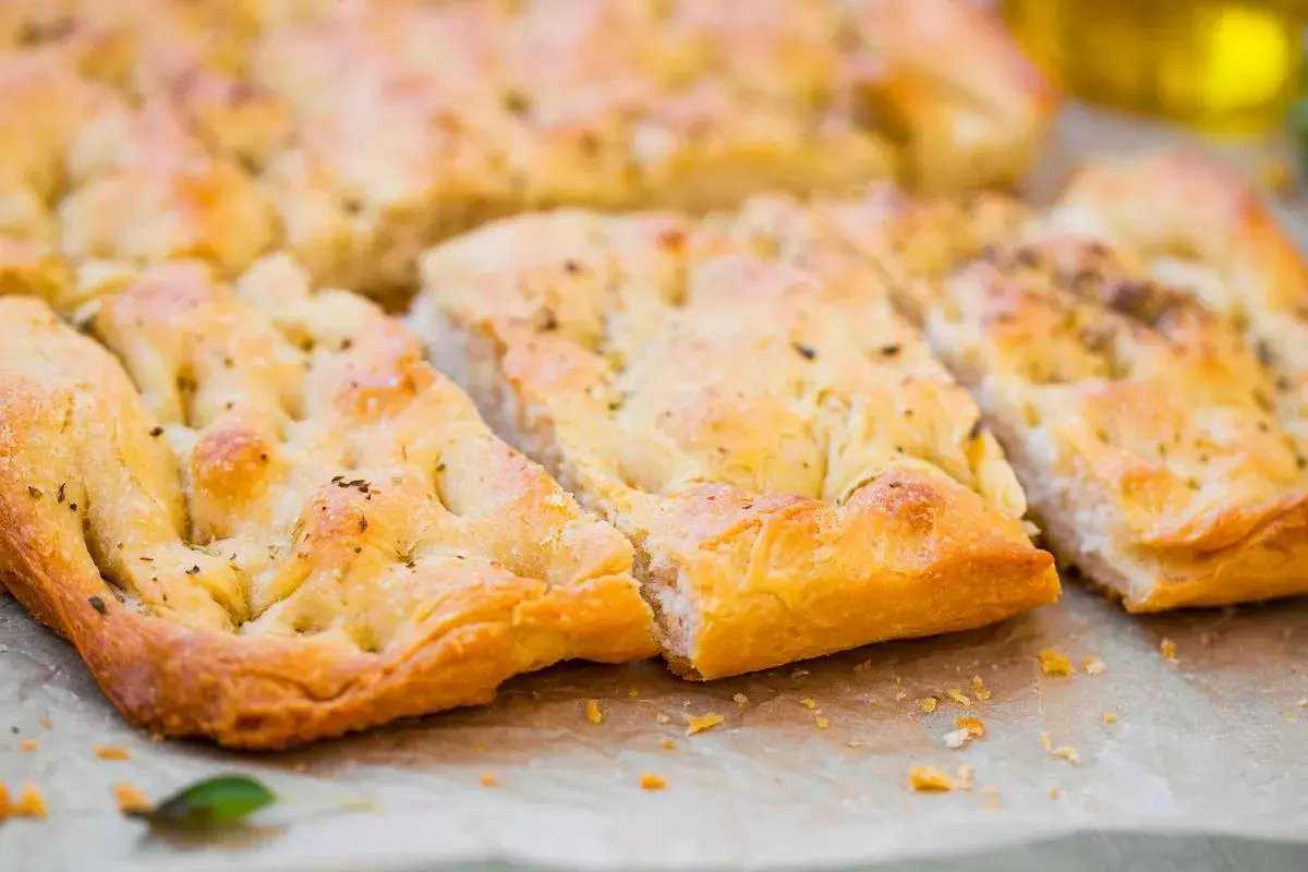 Focaccia senza lievito dorata e fragrante, tagliata a pezzi, con erbe aromatiche e un filo d'olio d'oliva.