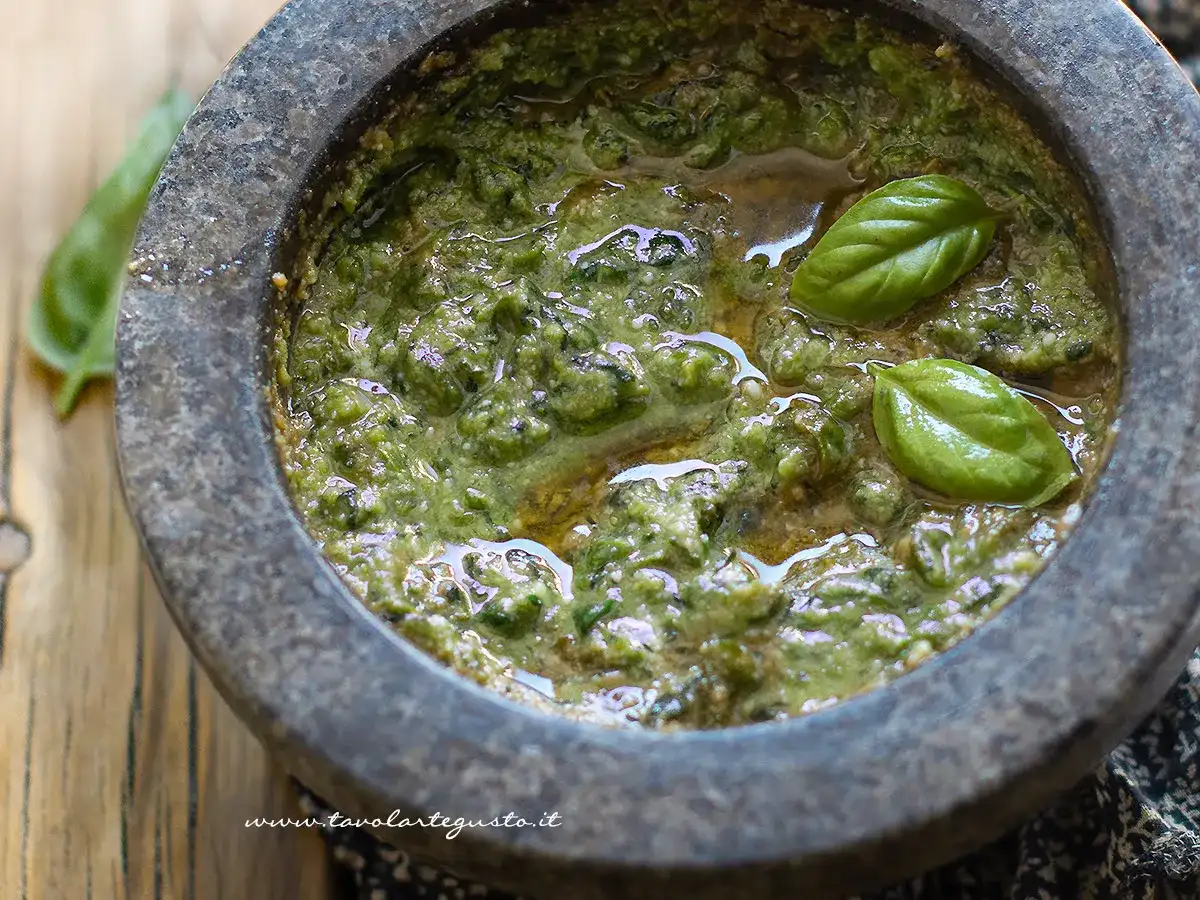 Pesto alla genovese appena preparato nel mortaio, con foglie di basilico fresco che galleggiano sull'olio.