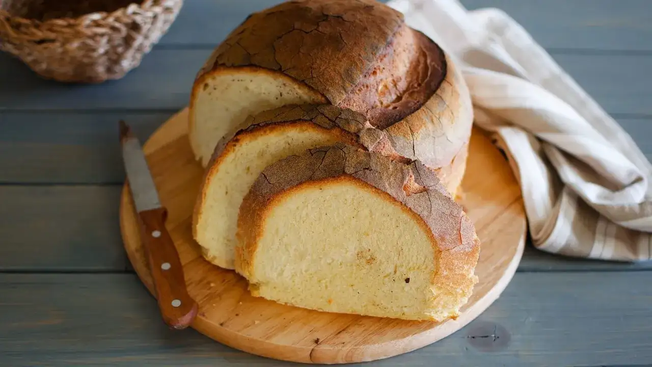 Pane di semola rustico, affettato su tagliere di legno, con coltello e tovagliolo a righe.