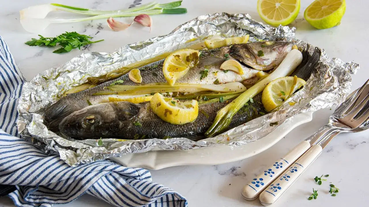 Branzino al cartoccio pronto per essere gustato, con limone, erbe aromatiche e cipollotti.