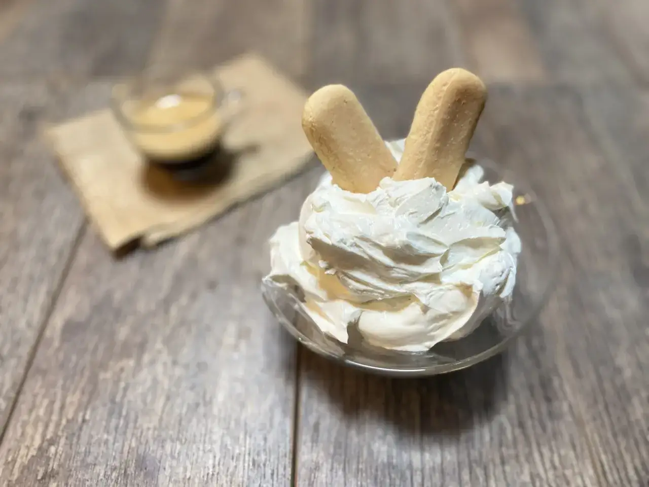 Coppa di crema al mascarpone senza uova, soffice e invitante, con savoiardi e una tazzina di caff&egrave; sullo sfondo.