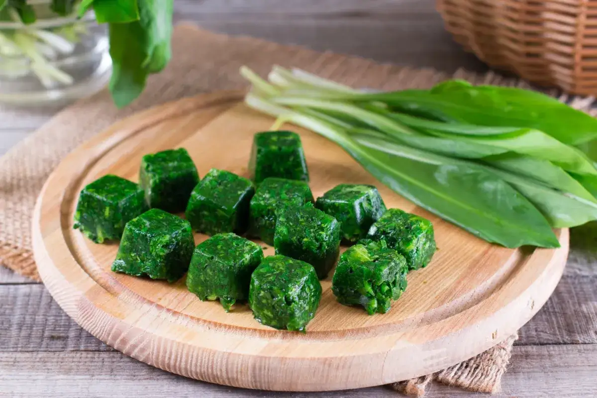 Cubetti di spinaci surgelati in padella, pronti per essere cucinati. Accanto, un mazzo di spinaci freschi.