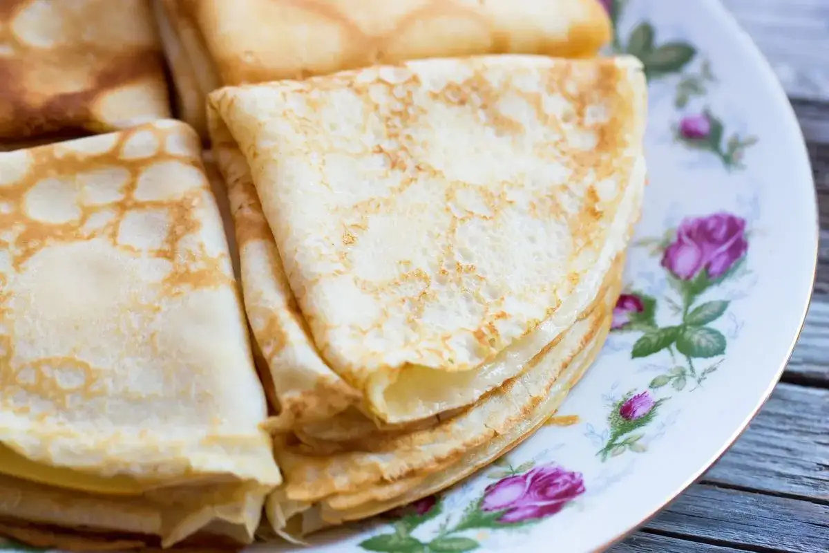 Delicate crepes senza uova, piegate e impilate su un piatto fiorito. Perfette per una colazione leggera o un dolce sfizioso.