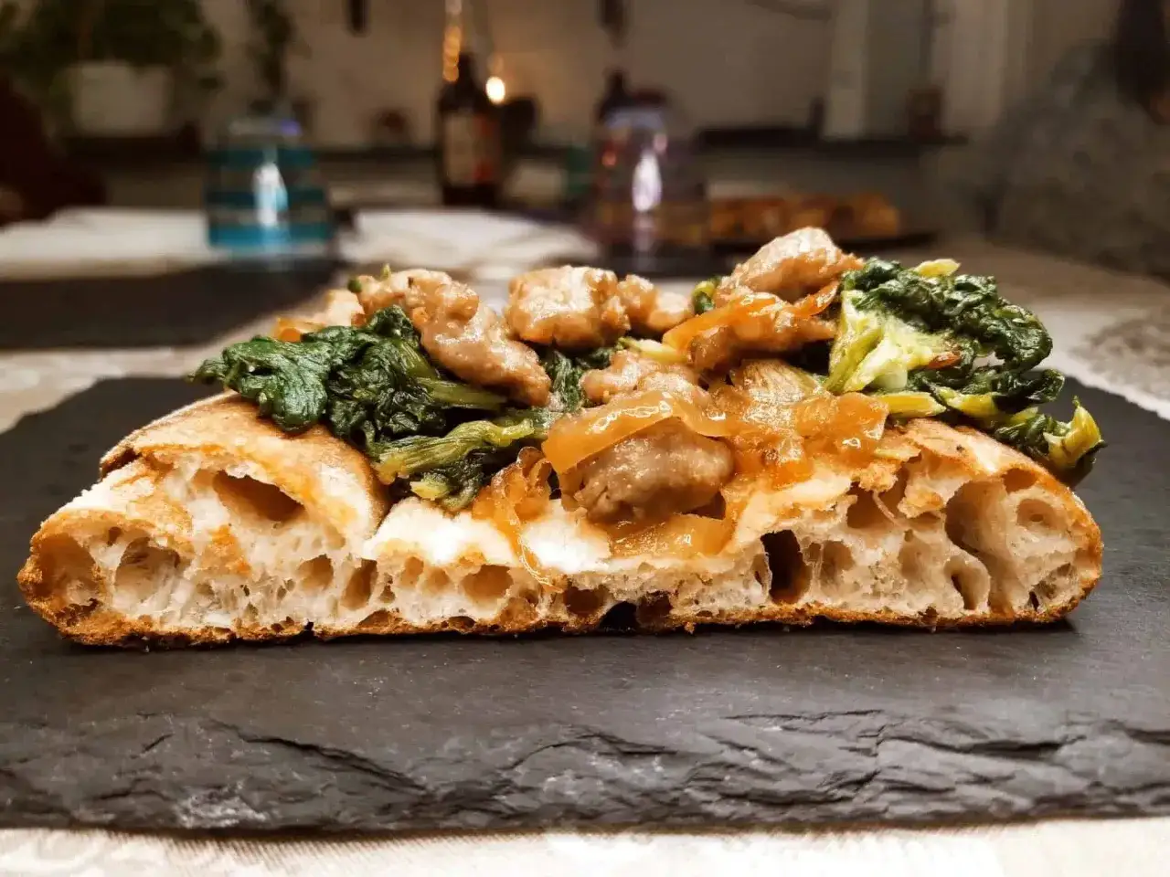 Fetta di pizza in teglia con impasto alveolato, condita con verdure verdi e pezzetti di carne saporiti.