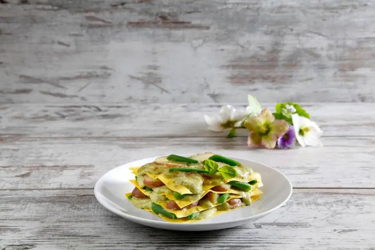 Lasagne al pesto con fagiolini e patate, un piatto colorato e gustoso su un tavolo di legno.