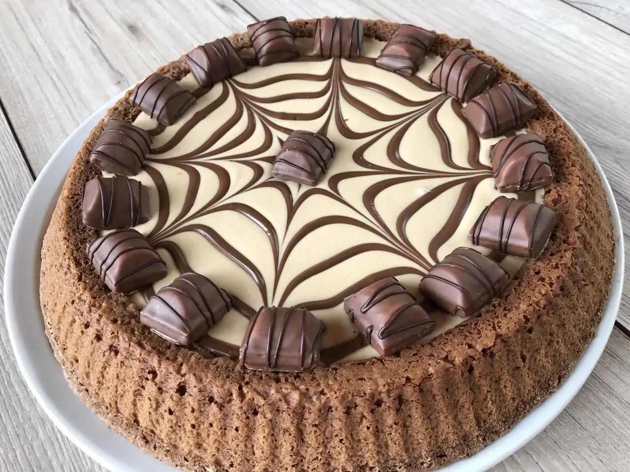 Torta con decorazione a ragnatela in crema chiara e scura, guarnita con pezzi di torta kinder bueno.