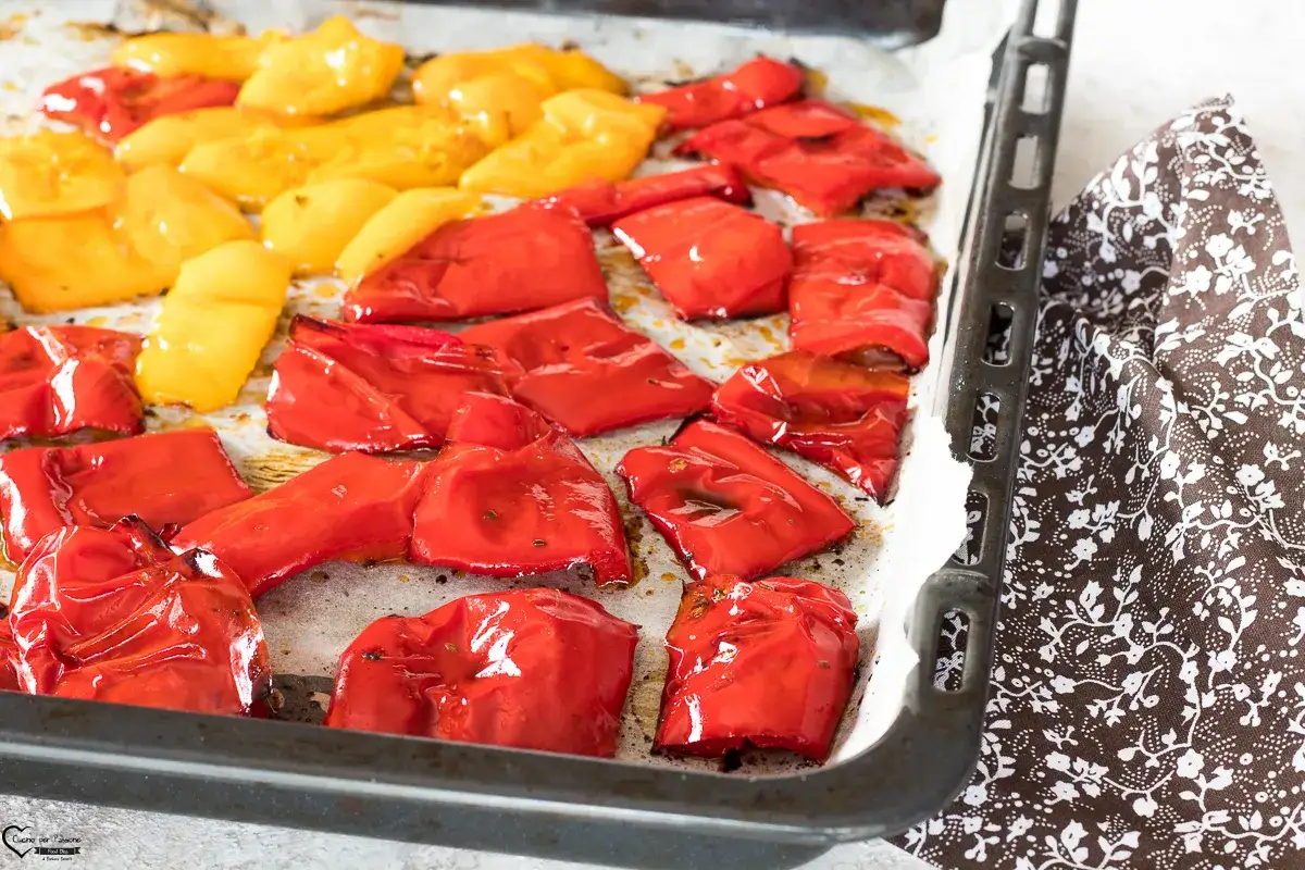 Peperoni al forno, rossi e gialli, cotti su carta forno in una teglia, pronti per essere gustati.