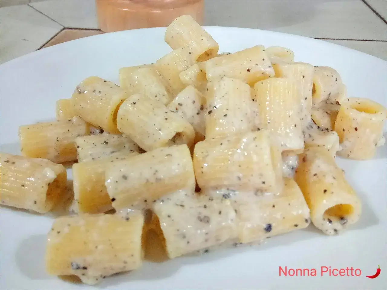 Un piatto di rigatoni cremosi al cacio e pepe, conditi con abbondante pepe nero macinato.