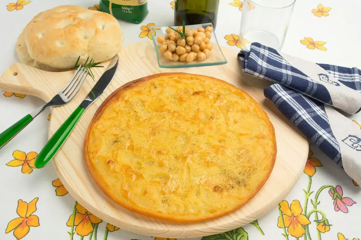 Farinata di ceci appena sfornata in padella, con ceci, pane e posate.