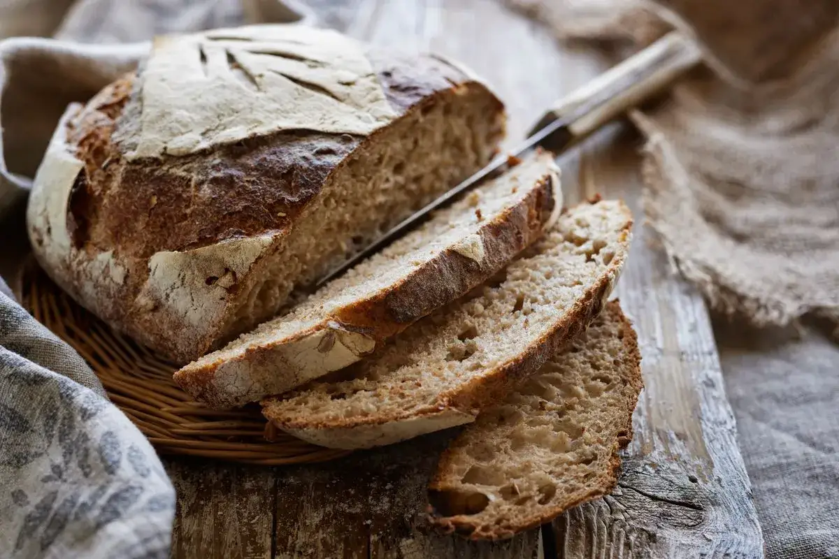 Pane fatto in casa con lievito di birra, tagliato a fette su un tagliere di legno. La crosta è dorata e croccante, l'interno morbido e alveolato.
