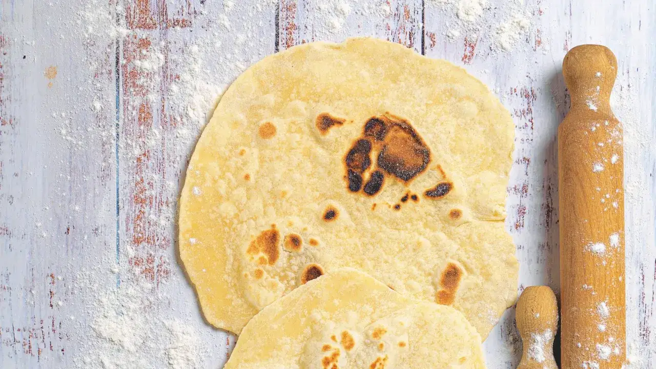 Piadina fatta in casa, appena sfornata, con macchie dorate e un mattarello pronto all'uso su un tavolo infarinato.