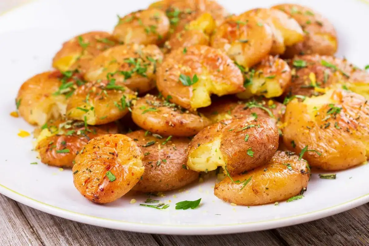 Patate novelle croccanti e dorate, appena sfornate dalla friggitrice ad aria, cosparse di erbe aromatiche fresche.