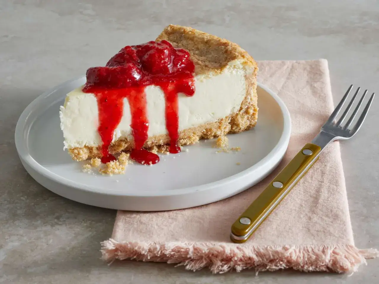 Una fetta di cheesecake cremosa con una base croccante, ricoperta da un goloso coulis di fragole che cola.