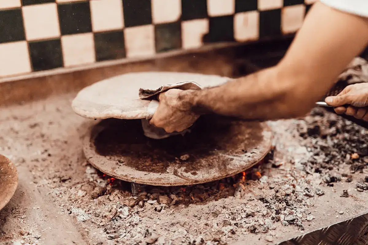 Mani esperte girano una torta al testo su un focolare ardente, tra cenere e calore.