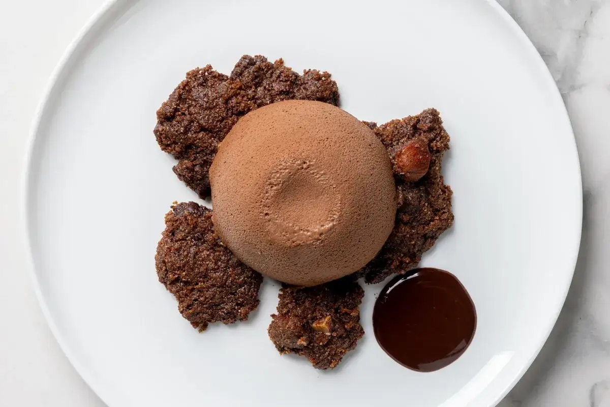 Delizioso semifreddo al cioccolato su un piatto bianco, accompagnato da croccanti biscotti al cacao e una salsa al cioccolato.