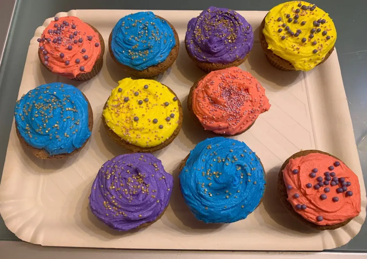 Dieci cupcake colorati con crema al burro, decorati con zuccherini e perline.