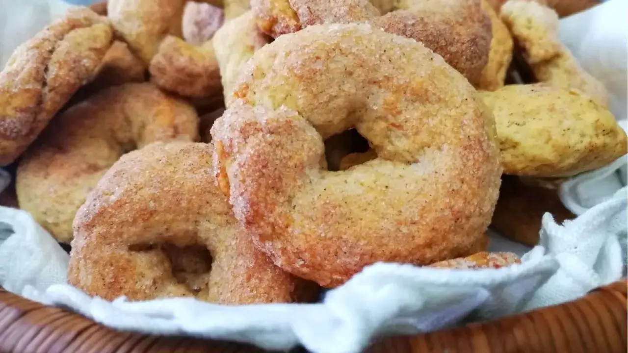Ciambelline al vino dorate e zuccherate, un dolce profumato in un cesto foderato di bianco.