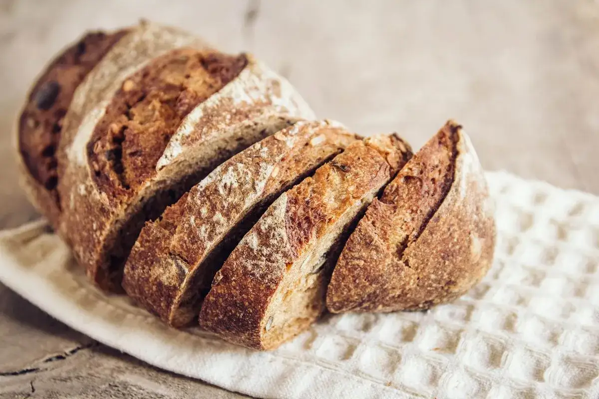 Fetta di pane di grano saraceno rustico, con crosta croccante e mollica scura e invitante, adagiata su un canovaccio bianco.