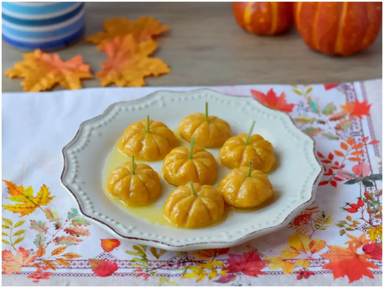 Gnocchi di zucca a forma di piccole zucche, serviti su un piatto bianco con un condimento dorato.